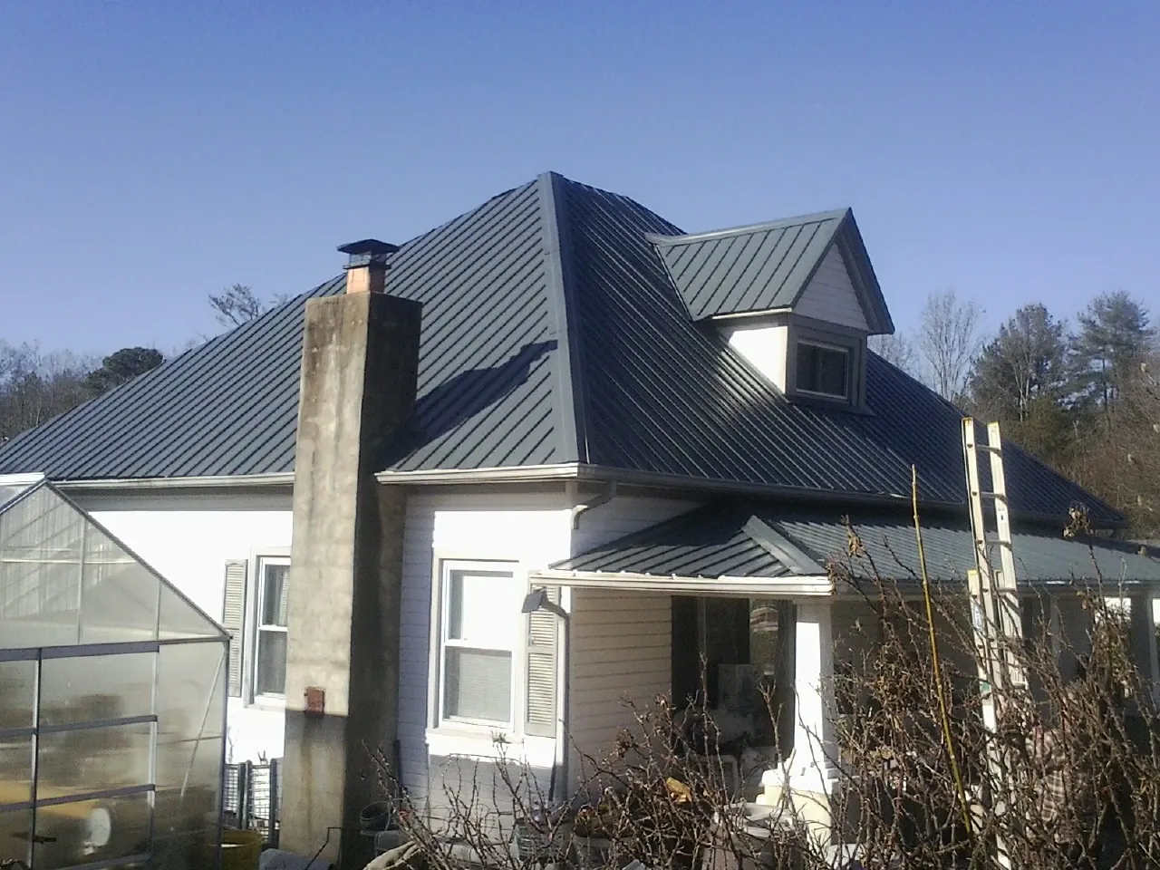 Dark blue standing seam metal roof on a white farmhouse with dormer in Greenfield