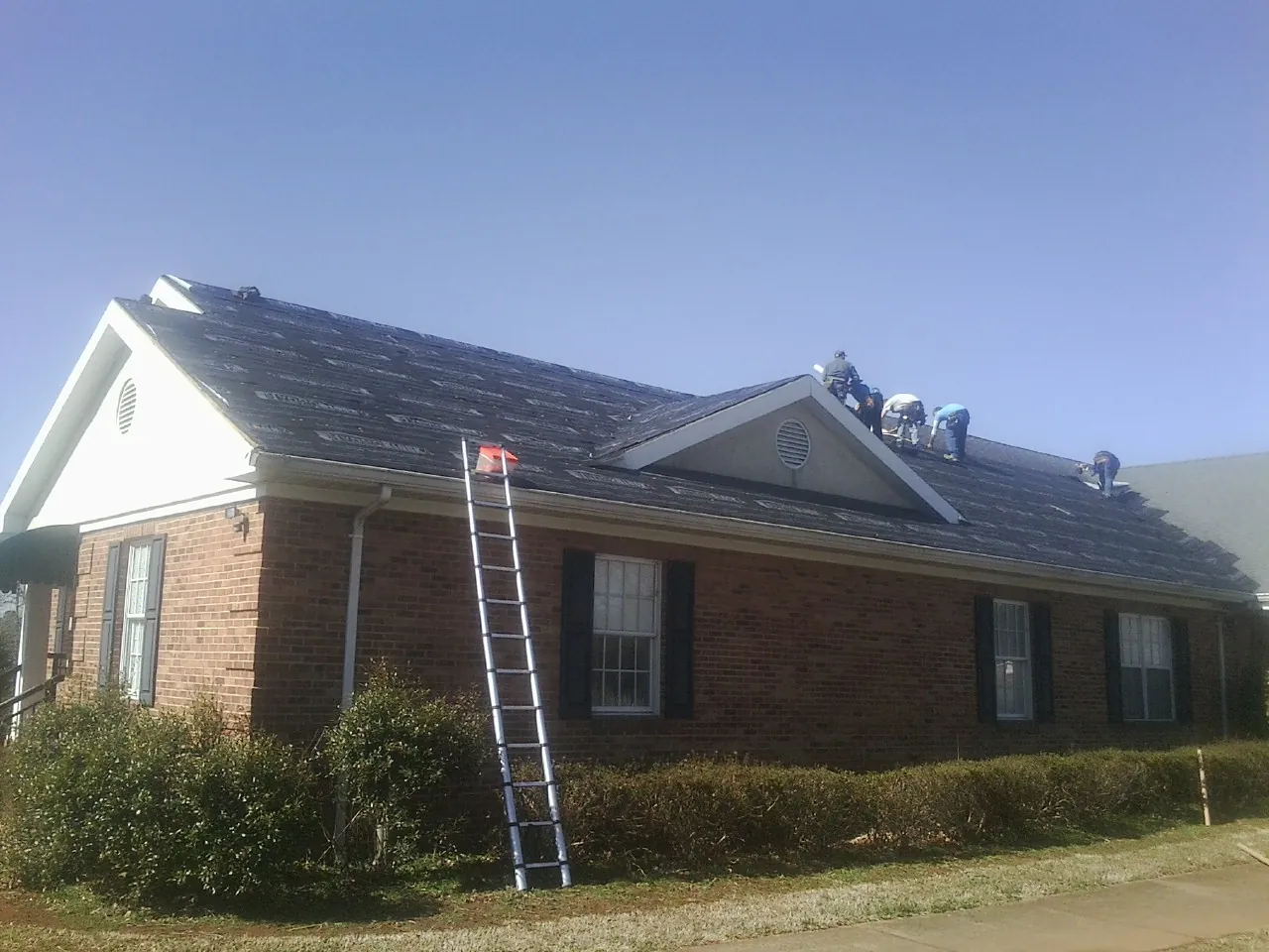 Crew tearing shingles off a brick ranch roof with a ladder set — Emergency Roof Repair work by our crew in Greenfield